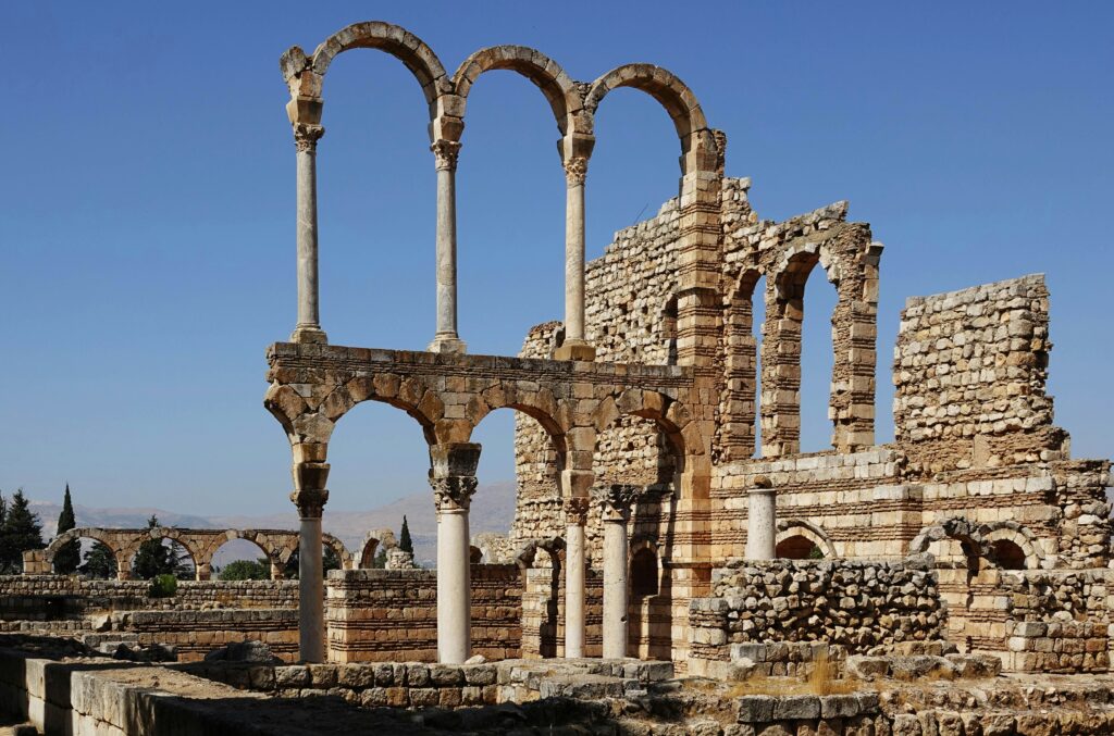 Ruins of the Umayyad city of Anjar in Lebanon, showing stone arches and columns of a Roman-influenced structure under a clear blue sky.