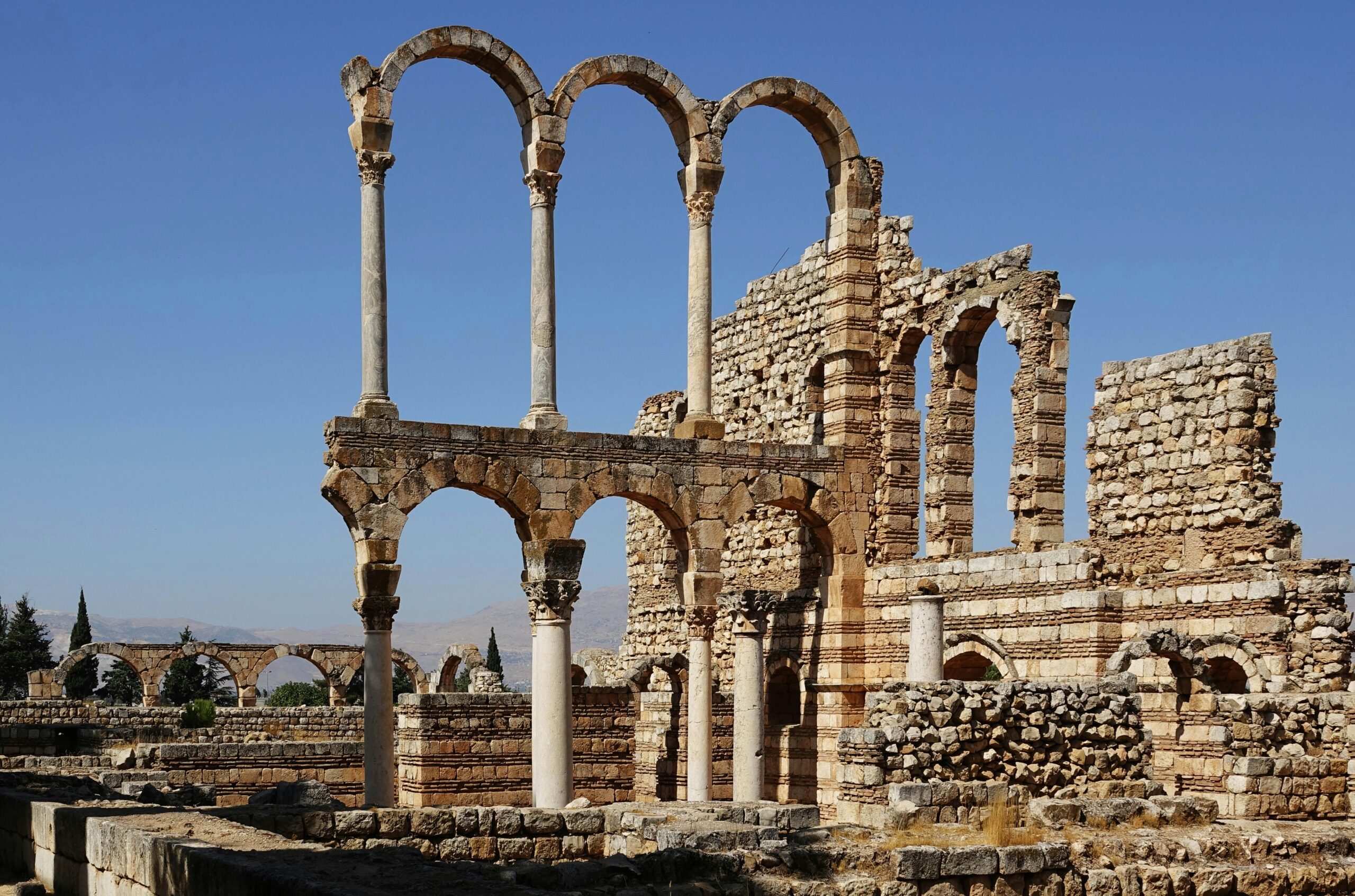 Ruins of the Umayyad city of Anjar in Lebanon, showing stone arches and columns of a Roman-influenced structure under a clear blue sky.