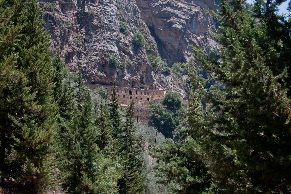 Monastery buildings set into the rocky cliffs of the Qadisha Valley, Lebanon, surrounded by dense forest.