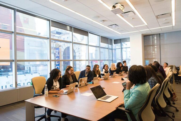 Group of professionals seated around a conference table in a modern meeting room, working collaboratively on laptops.