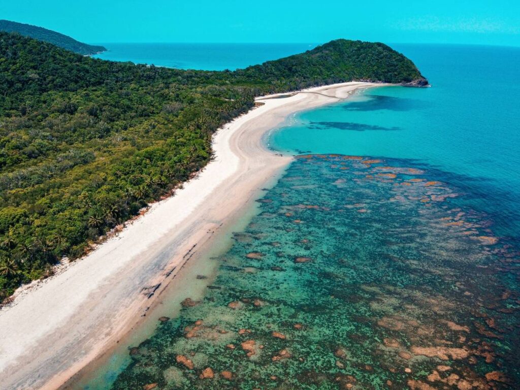 Aerial view of a tropical coastline with sandy beach, forest, and coral reef.