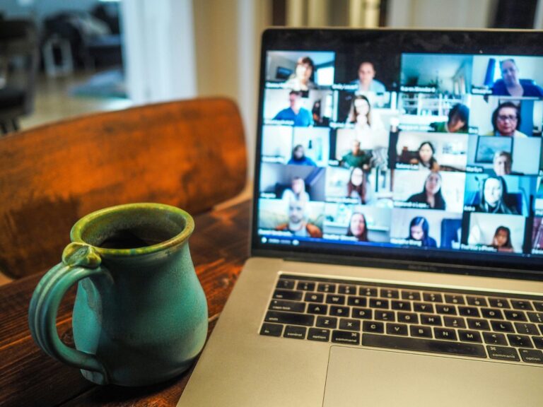 Laptop displaying a virtual meeting with multiple participants, next to a coffee mug on a desk.